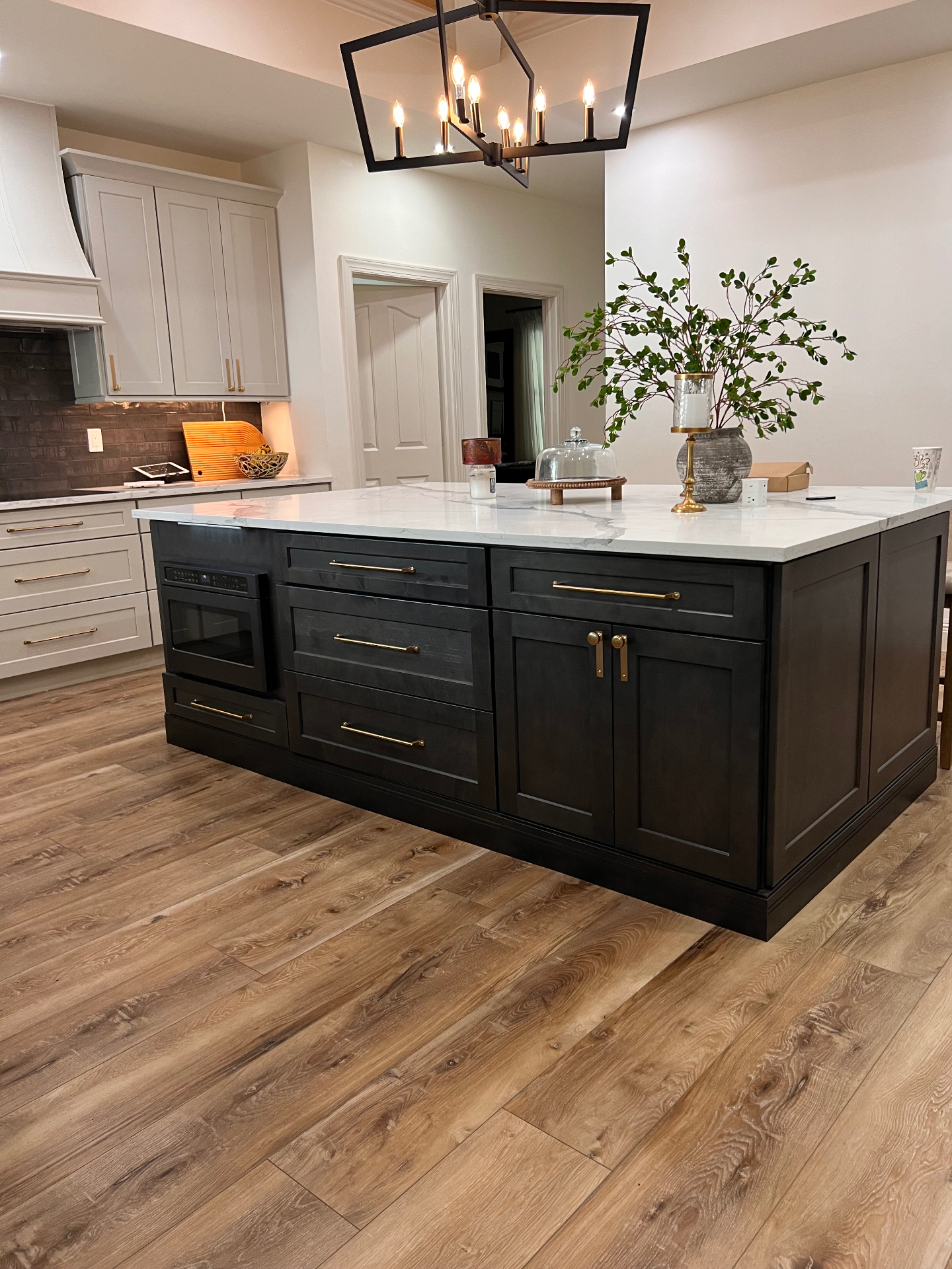 Finished whole-home renovation kitchen with dark island, brass hardware, and quartz waterfall countertop in Naples, FL