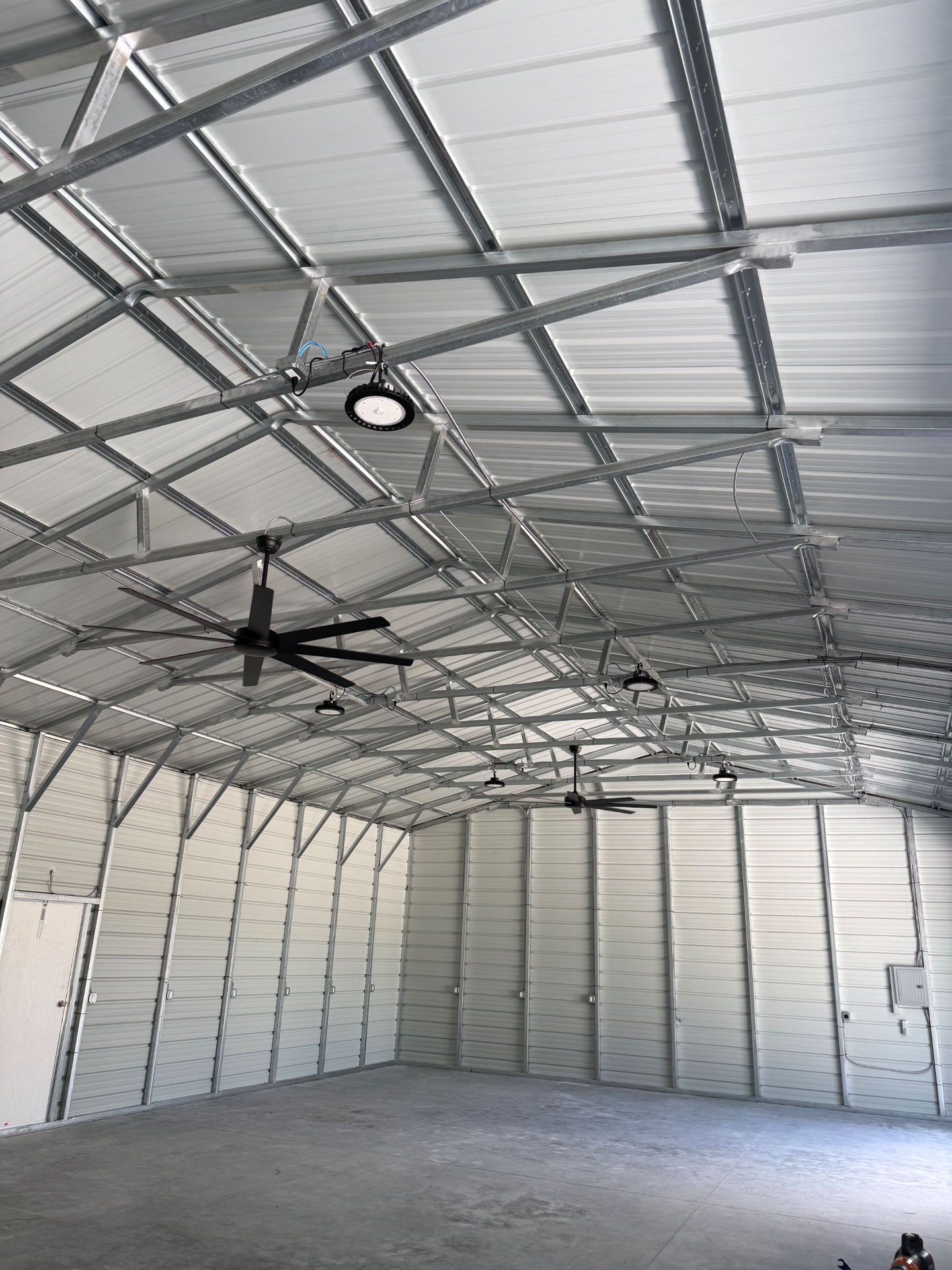 Interior of finished steel building showing trusses, fans, and high-bay lighting
