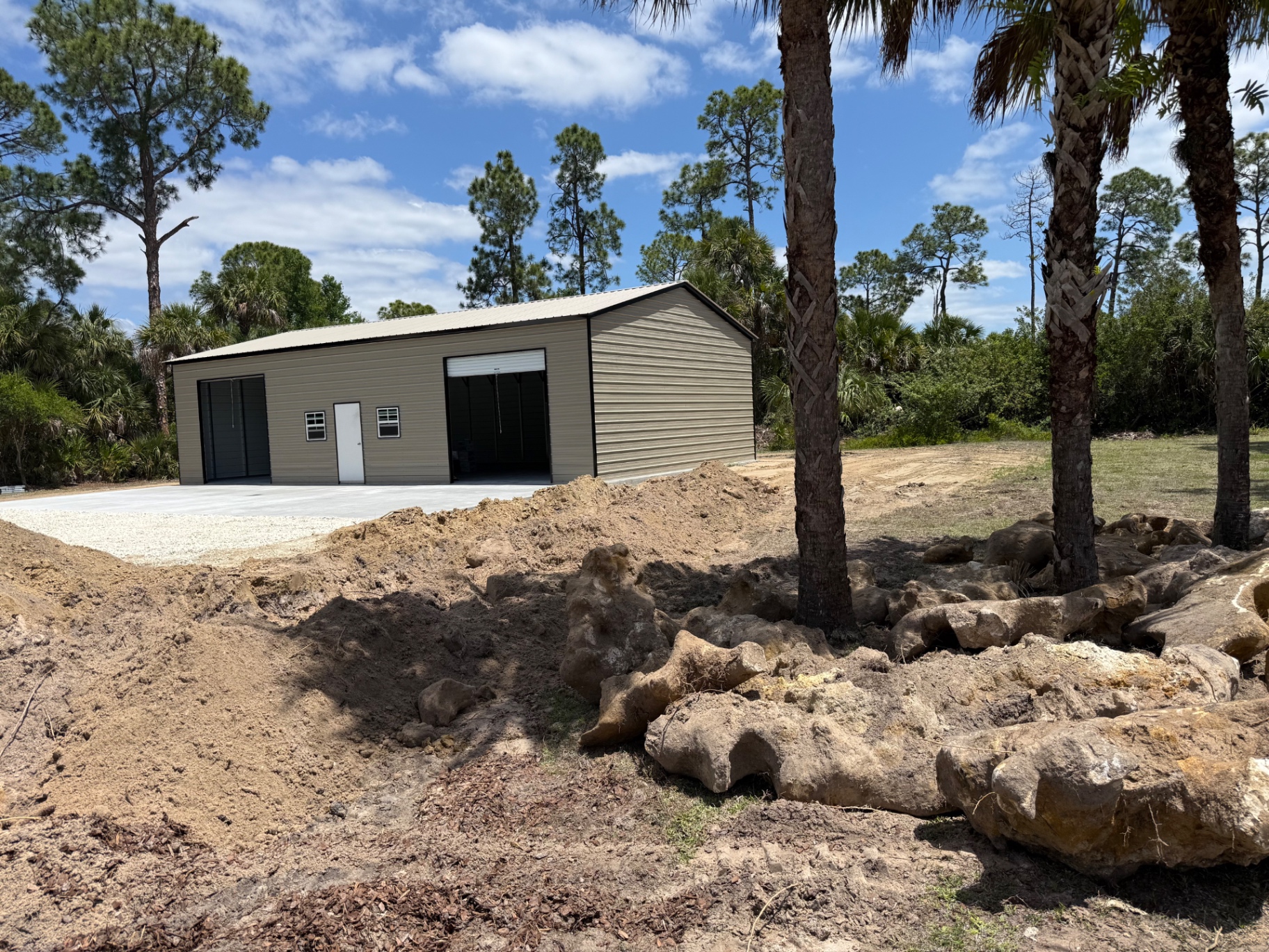 Completed tan steel garage with roll-up doors on prepared site in Naples, FL